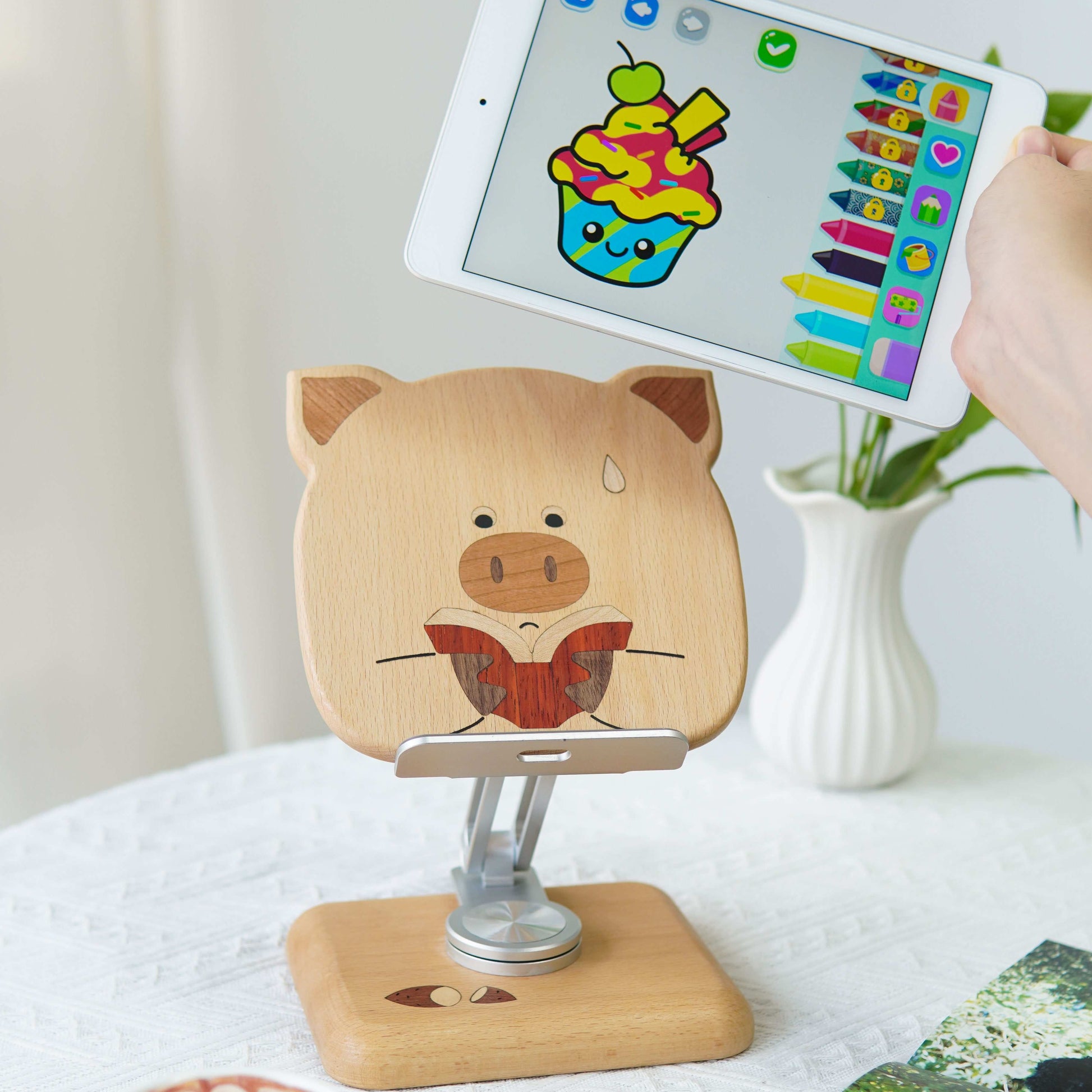 Wooden pig-shaped phone stand with tablet on a white surface with a cup of coffee.