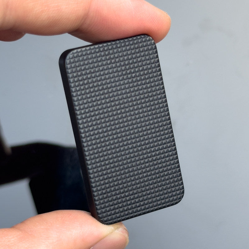 Hand holding a textured black rectangular object against a gray background