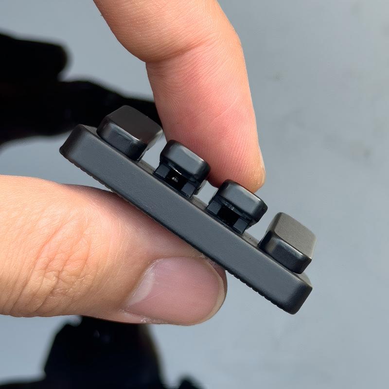 Hand holding a small metallic device with multiple components against a blurred background