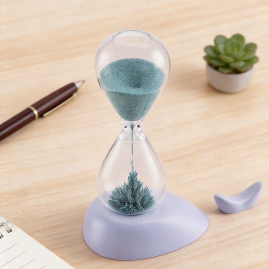 Hourglass with sand and decorative elements on a wooden surface with a pen and plants.