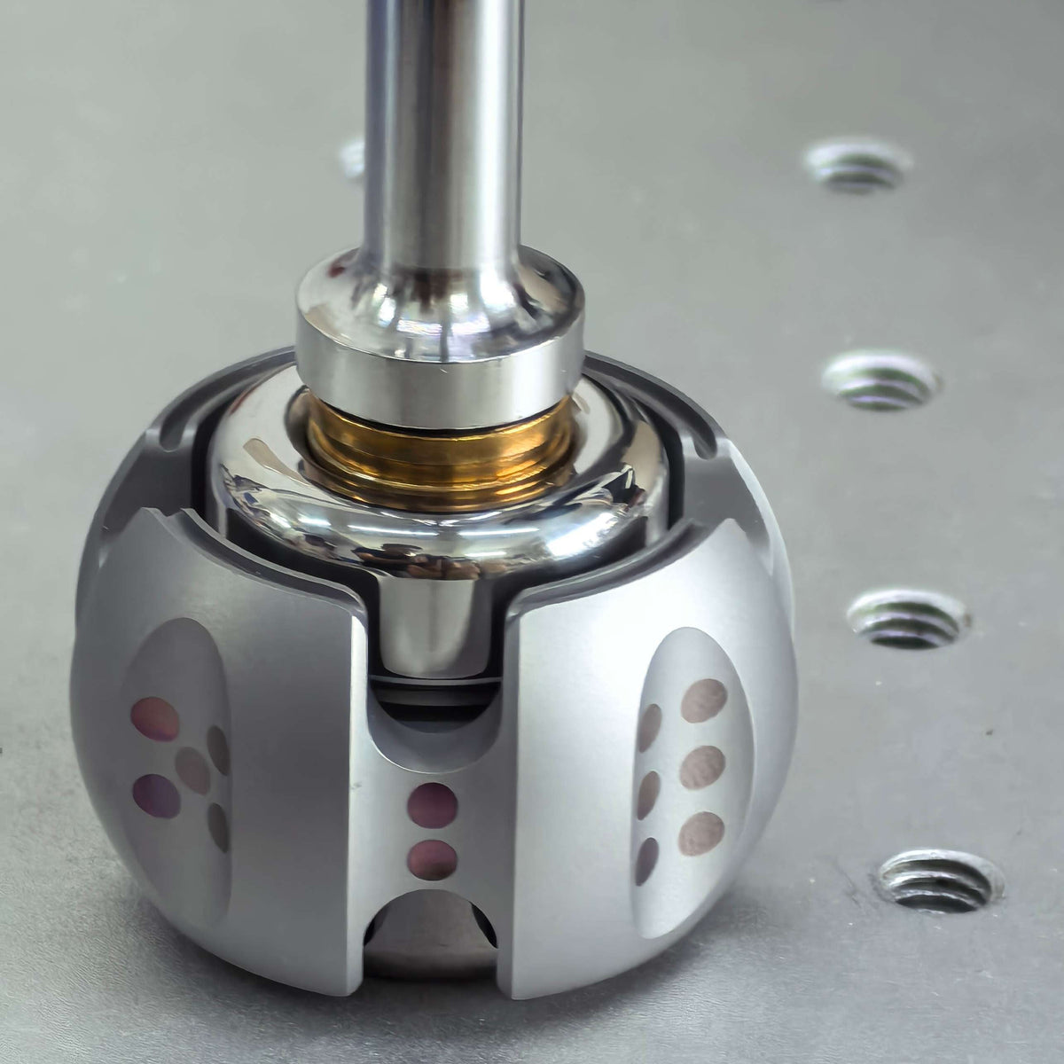 A close-up of a metallic dental drill bit attachment mounted on a silver drill shaft, positioned over a perforated metal work surface.